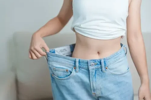 Person holding oversized jeans, indicating weight loss progress.