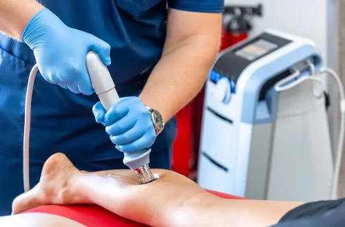 Technician using a device for shockwave treatment on a patient's leg.